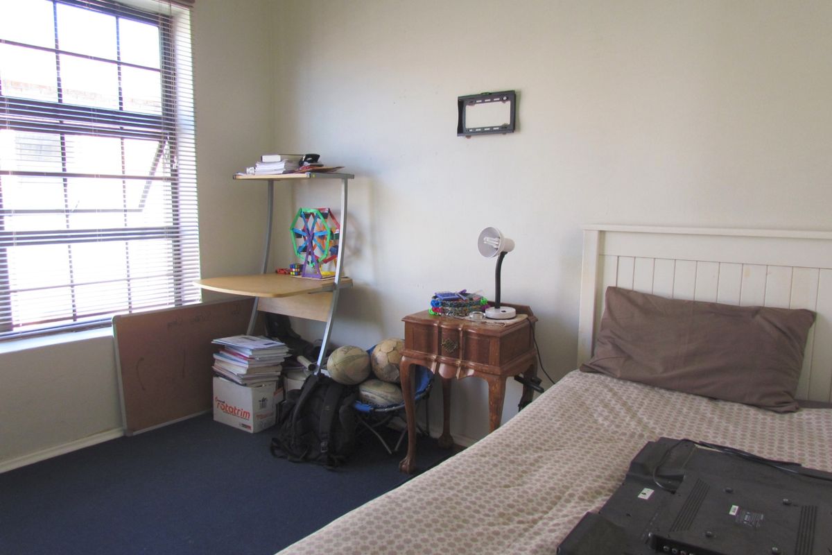 A functional bedroom featuring carpeted flooring and a large window with venetian blinds, providing natural light to the space.
