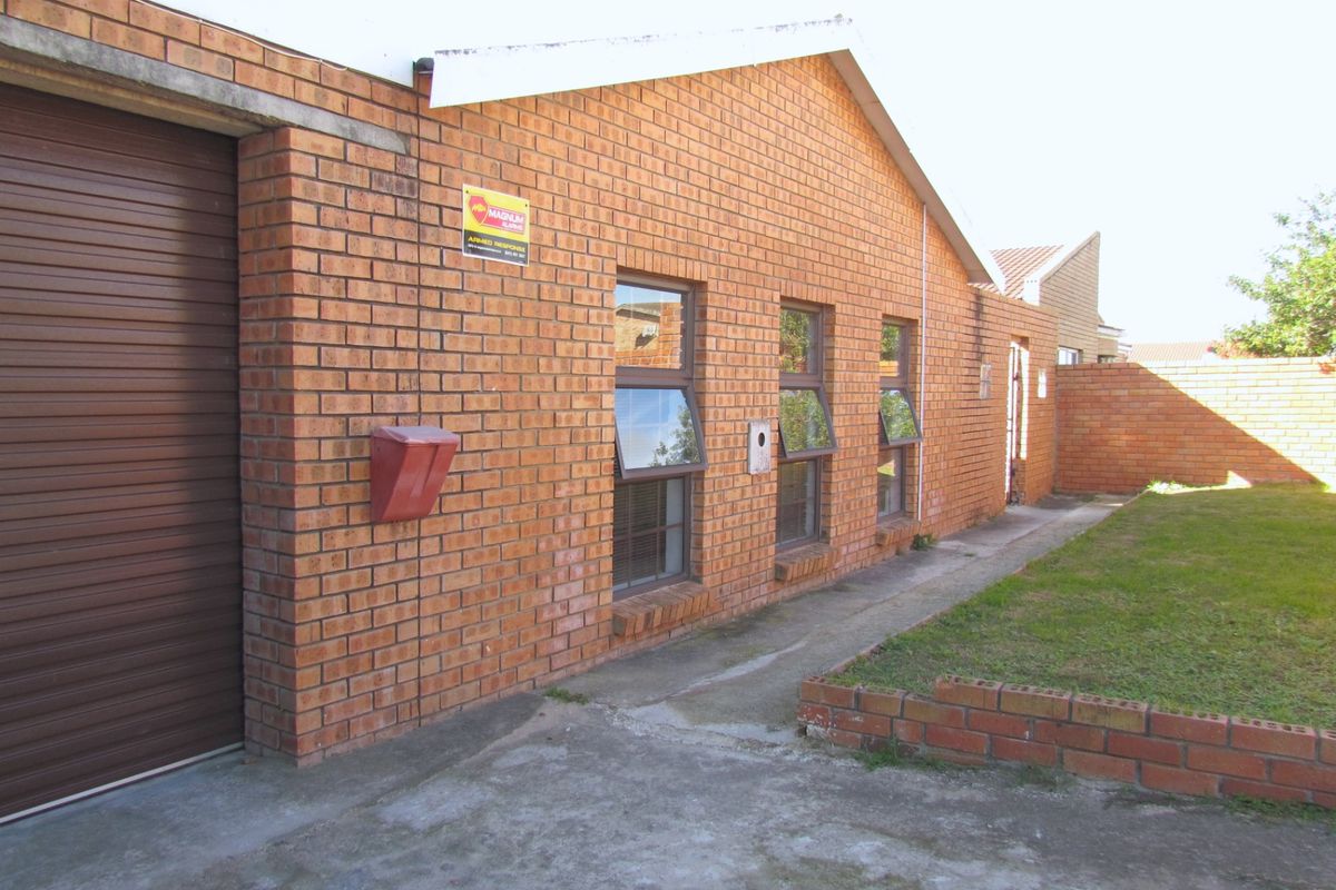 Rear exterior view of the property featuring face brick construction, a roller shutter garage door, top-hung windows, and a small lawn area.