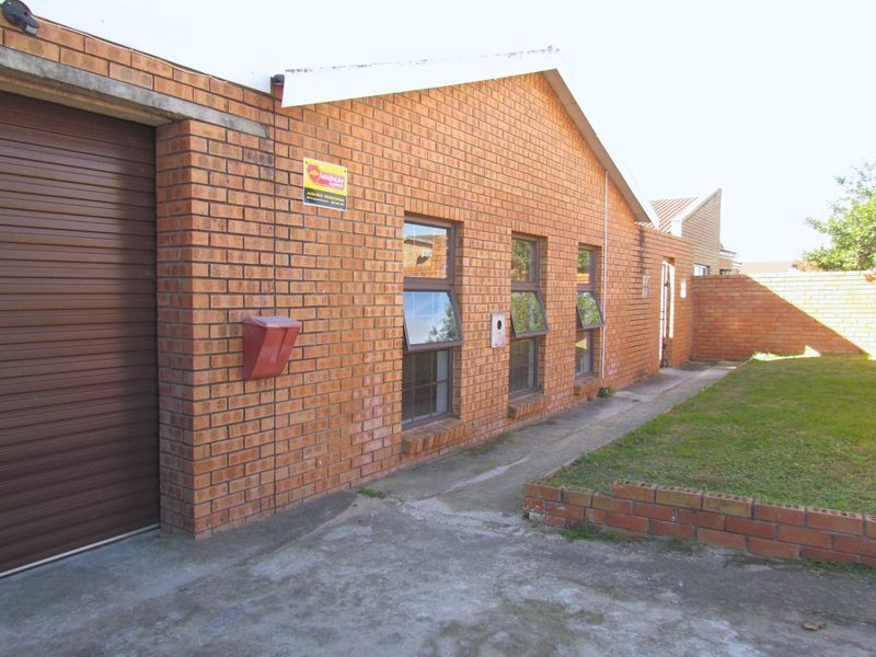 Rear exterior view of the property featuring face brick construction, a roller shutter garage door, top-hung windows, and a small lawn area.
