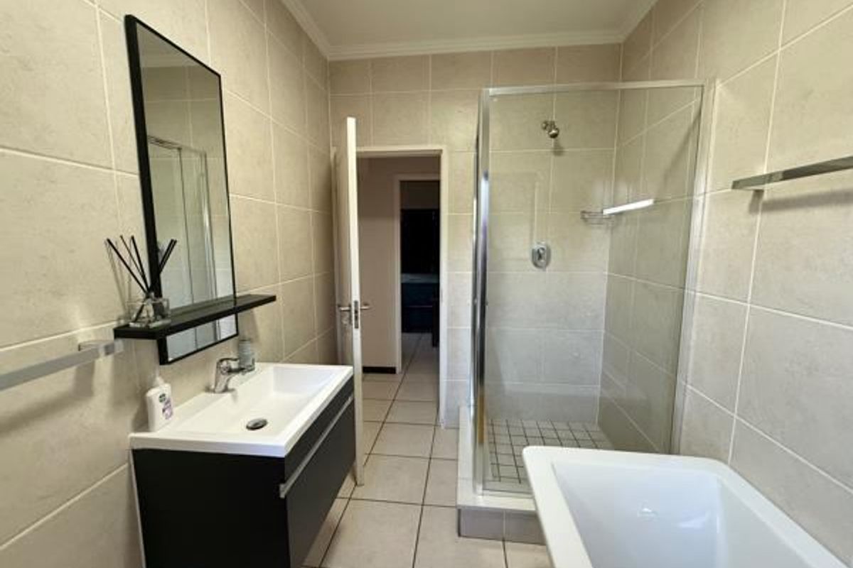 Modern bathroom featuring a wall-mounted vanity, glass shower enclosure, and a freestanding bathtub with neutral ceramic tiling throughout.