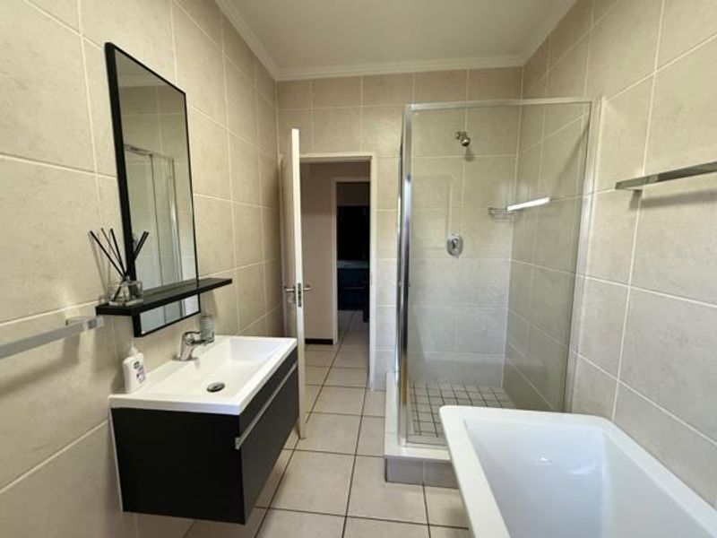Modern bathroom featuring a wall-mounted vanity, glass shower enclosure, and a freestanding bathtub with neutral ceramic tiling throughout.
