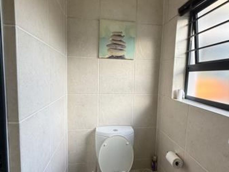 A compact bathroom featuring floor-to-ceiling neutral tiling, a standard toilet, and a window with security bars.