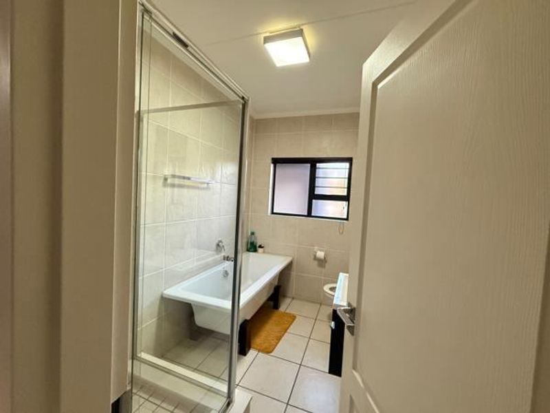 A functional bathroom featuring a freestanding bathtub, a separate glass-enclosed shower, and neutral wall and floor tiling.