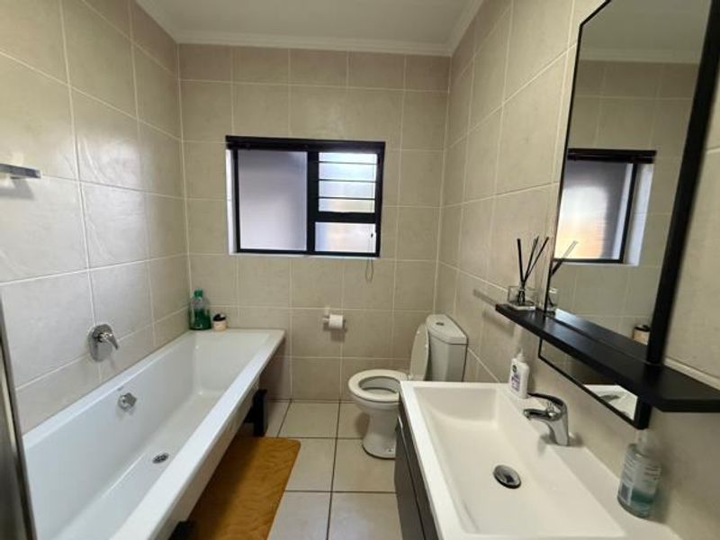 A clean and functional bathroom featuring a bathtub, toilet, and a modern vanity basin with a wall-mounted mirror and tiled finishes.