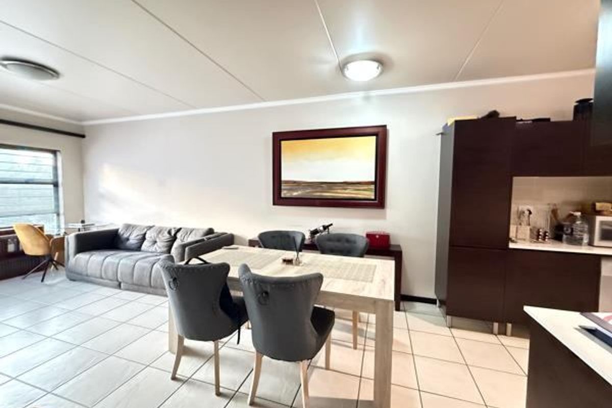 An open-plan living and dining area featuring tiled flooring and integrated kitchen cabinetry, providing a functional and connected layout for modern apartment living.