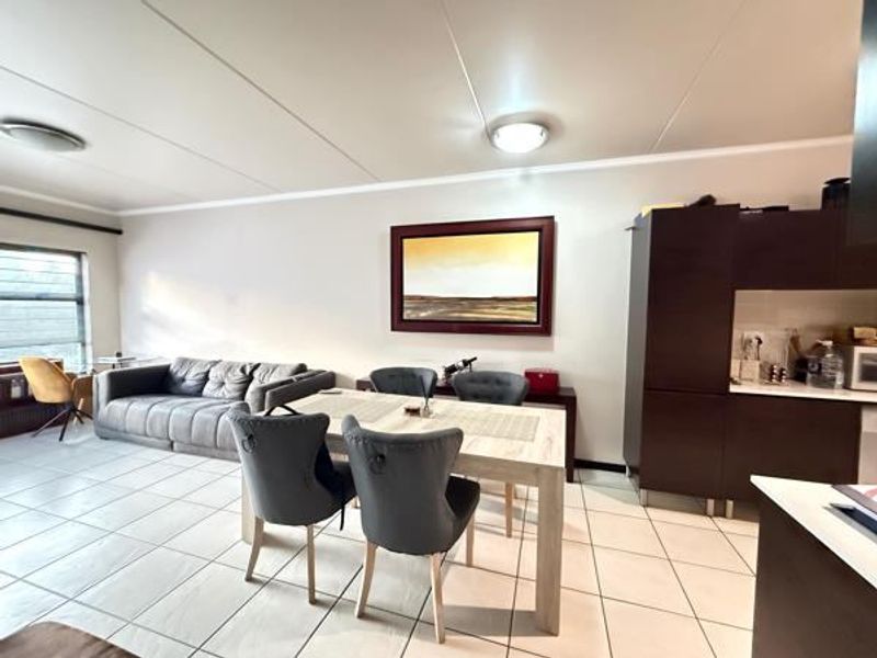 An open-plan living and dining area featuring tiled flooring and integrated kitchen cabinetry, providing a functional and connected layout for modern apartment living.