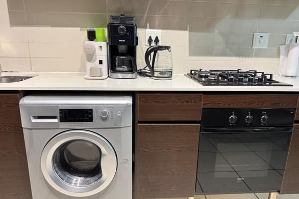 A functional kitchen area featuring dark wood cabinetry, stone countertops, a gas hob, built-in oven, and an integrated washing machine.