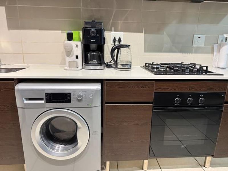 A functional kitchen area featuring dark wood cabinetry, stone countertops, a gas hob, built-in oven, and an integrated washing machine.