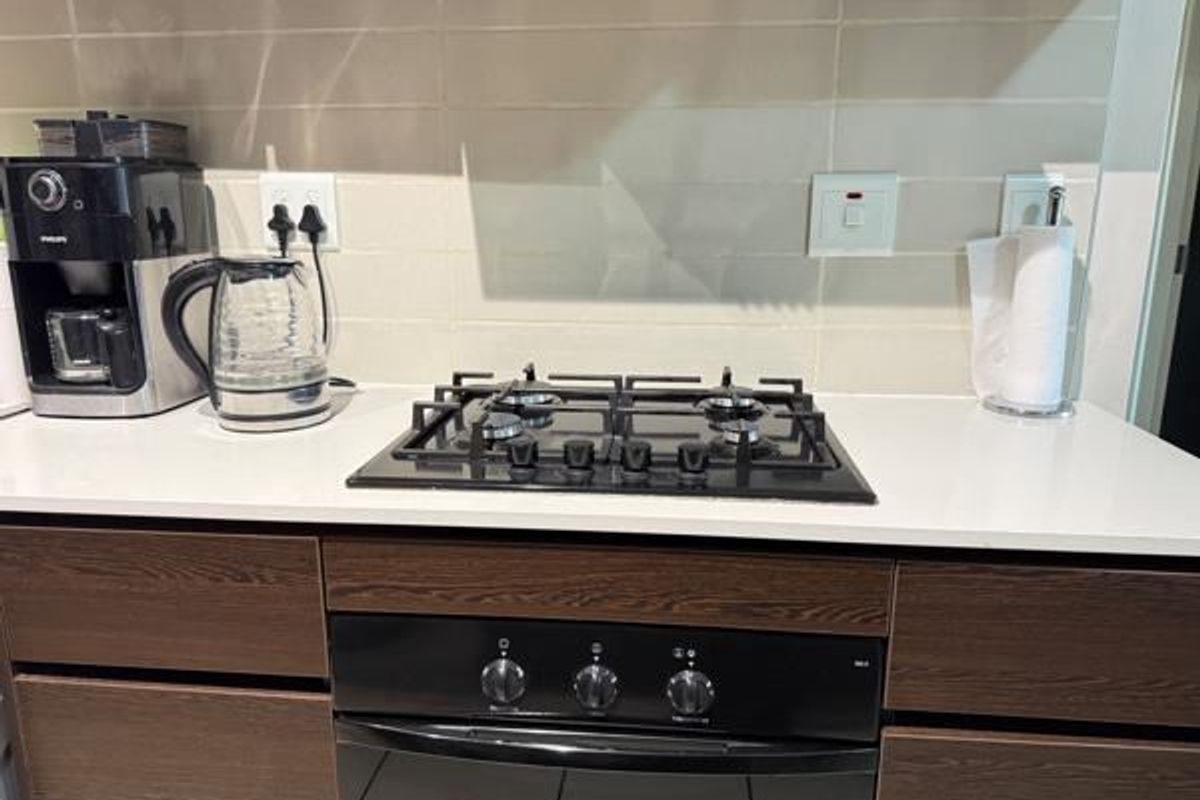 Modern kitchen area featuring a built-in gas hob, integrated oven, stone countertops, and a clean tiled backsplash.