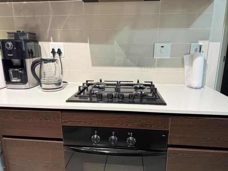 Modern kitchen area featuring a built-in gas hob, integrated oven, stone countertops, and a clean tiled backsplash.