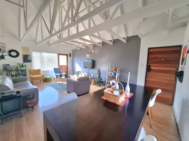 Spacious open-plan living and dining area featuring high vaulted ceilings with exposed white trusses, laminate flooring, and a solid timber entrance door.