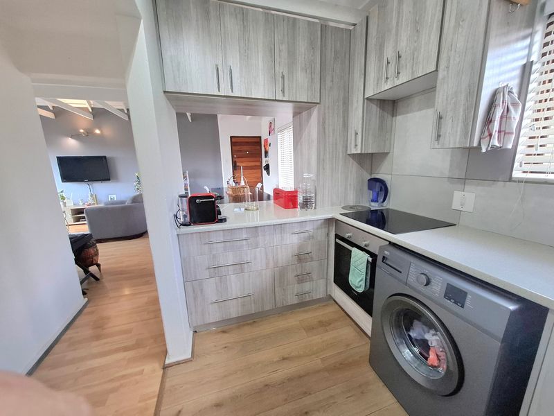Compact modern kitchen featuring light wood-grain cabinetry, laminate countertops, integrated washing machine, and built-in oven with electric hob.