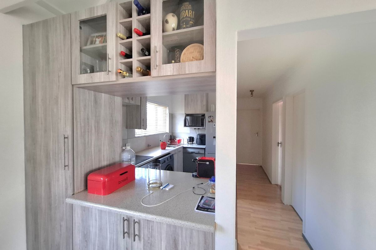 A functional kitchen featuring light wood-grain cabinetry, integrated wine storage, and laminate countertops, with an open-plan layout leading into a hallway.