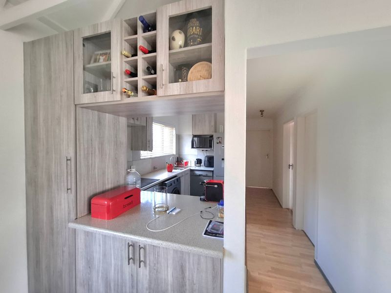 A functional kitchen featuring light wood-grain cabinetry, integrated wine storage, and laminate countertops, with an open-plan layout leading into a hallway.