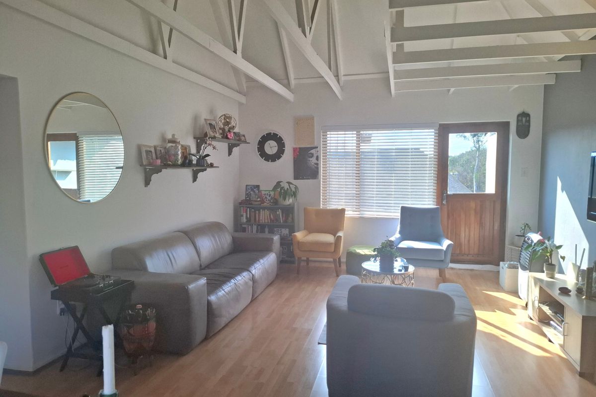 Spacious living room featuring high vaulted ceilings with exposed timber trusses, laminate flooring, and natural light through large windows and a timber door.