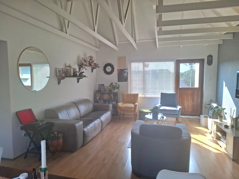 Spacious living room featuring high vaulted ceilings with exposed timber trusses, laminate flooring, and natural light through large windows and a timber door.
