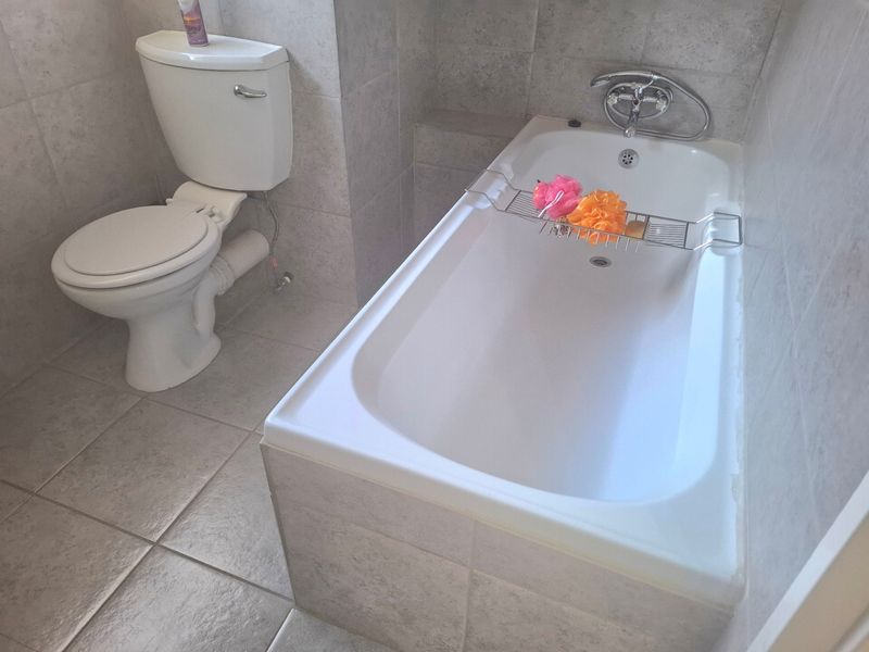 A functional bathroom featuring a standard bathtub and toilet with neutral wall and floor tiling.