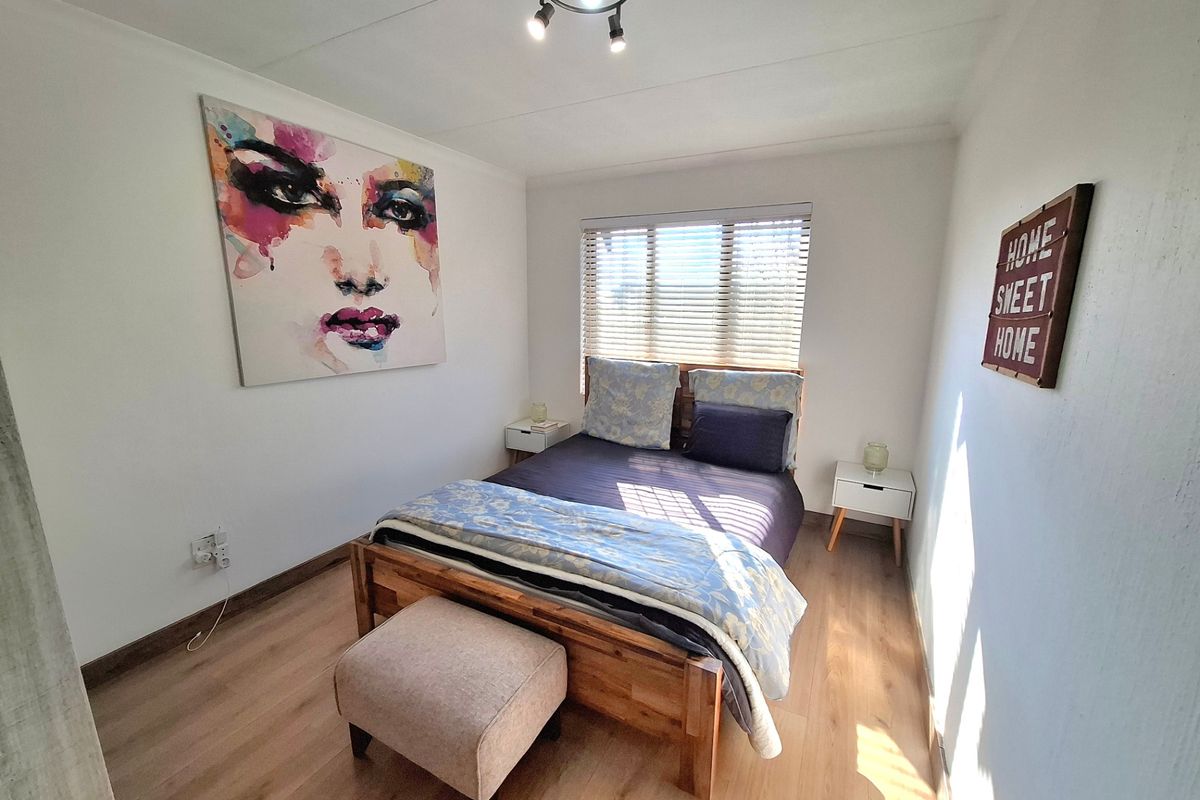 A well-lit bedroom featuring modern laminate flooring, neutral walls, and a functional window with venetian blinds.