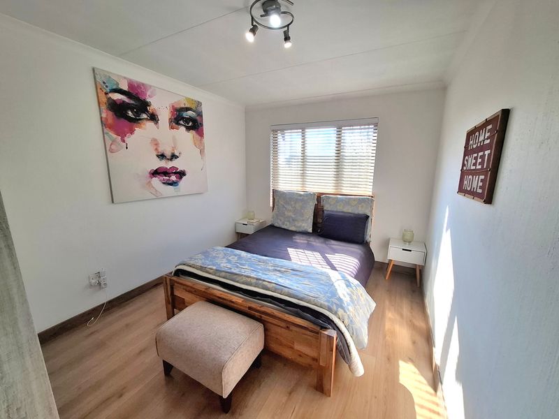 A well-lit bedroom featuring modern laminate flooring, neutral walls, and a functional window with venetian blinds.