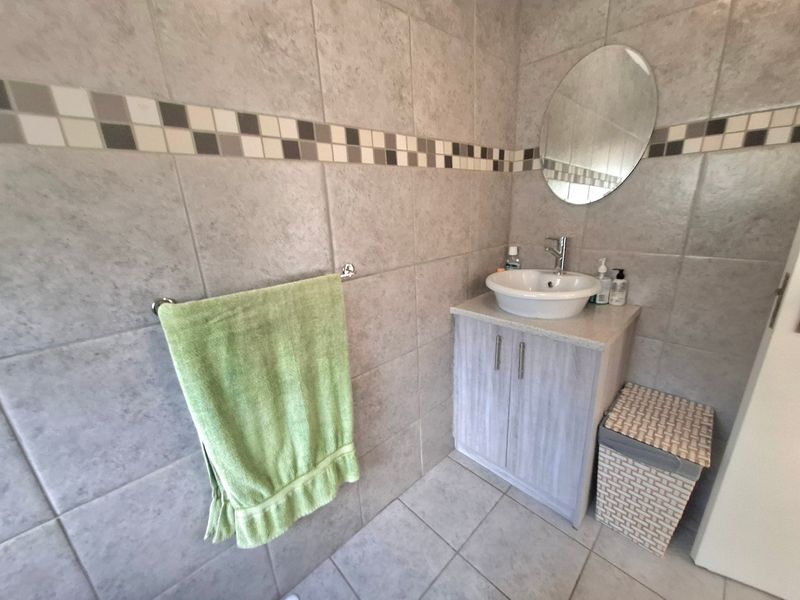 A functional bathroom featuring a vanity cabinet with a vessel sink, wall-mounted mirror, and neutral ceramic tiling throughout.