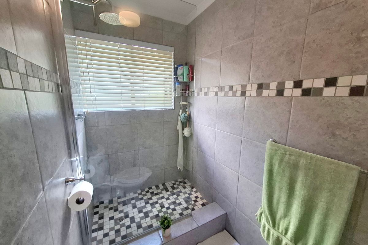 A functional bathroom featuring a walk-in shower with a glass screen, rainfall shower head, and neutral tiled finishes.