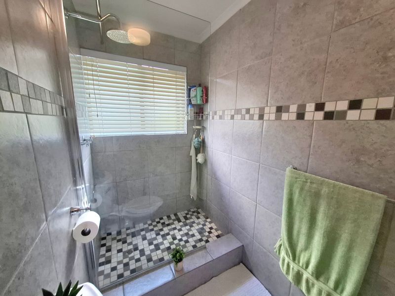 A functional bathroom featuring a walk-in shower with a glass screen, rainfall shower head, and neutral tiled finishes.