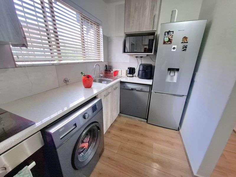 A functional scullery featuring laminate cabinetry, stone countertops, a stainless steel sink, and integrated appliance space for a dishwasher and washing machine.