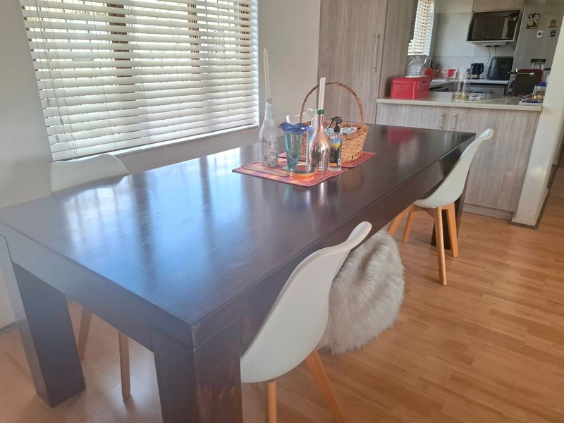 Open-plan dining area featuring laminate flooring and venetian blinds, seamlessly connected to a functional kitchen with built-in cabinetry and integrated microwave.