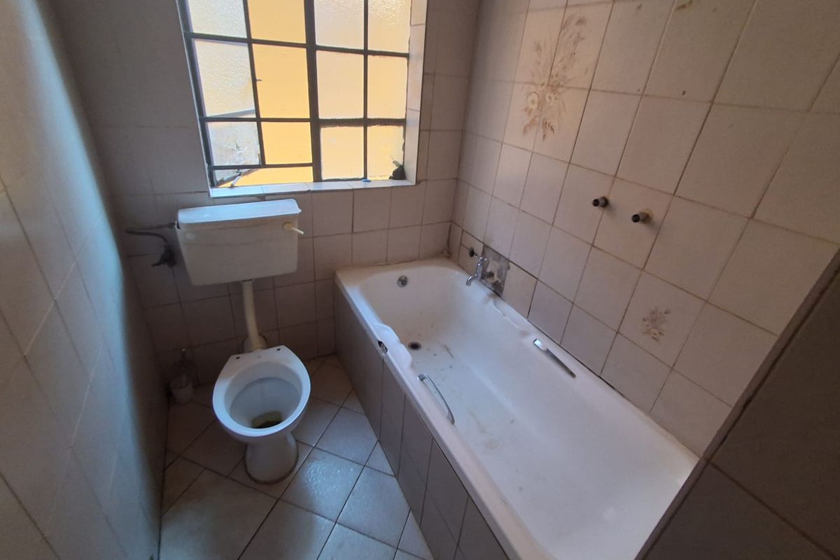 A dated bathroom featuring a standard bathtub, toilet, and tiled finishes, requiring renovation to modernize the space and address visible wear.
