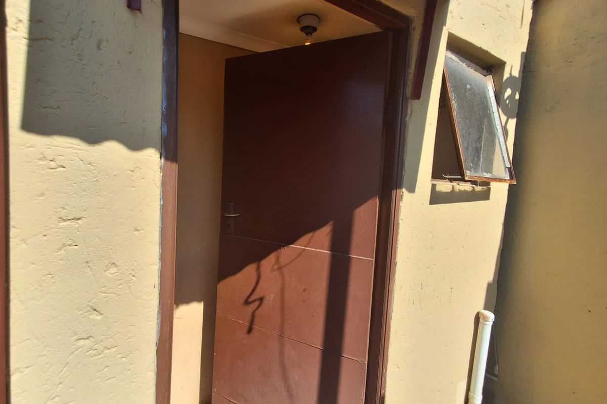 Exterior view of a rear entrance door with a small awning and adjacent top-hung window, showing signs of weathering and wear.