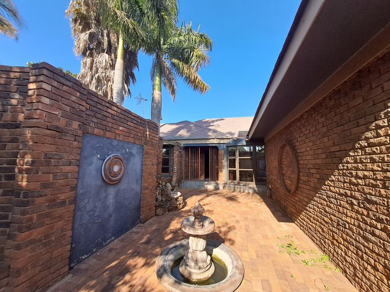 A private rear courtyard featuring face brick walls, paved flooring, and a central stone water fountain, providing a secluded outdoor space.