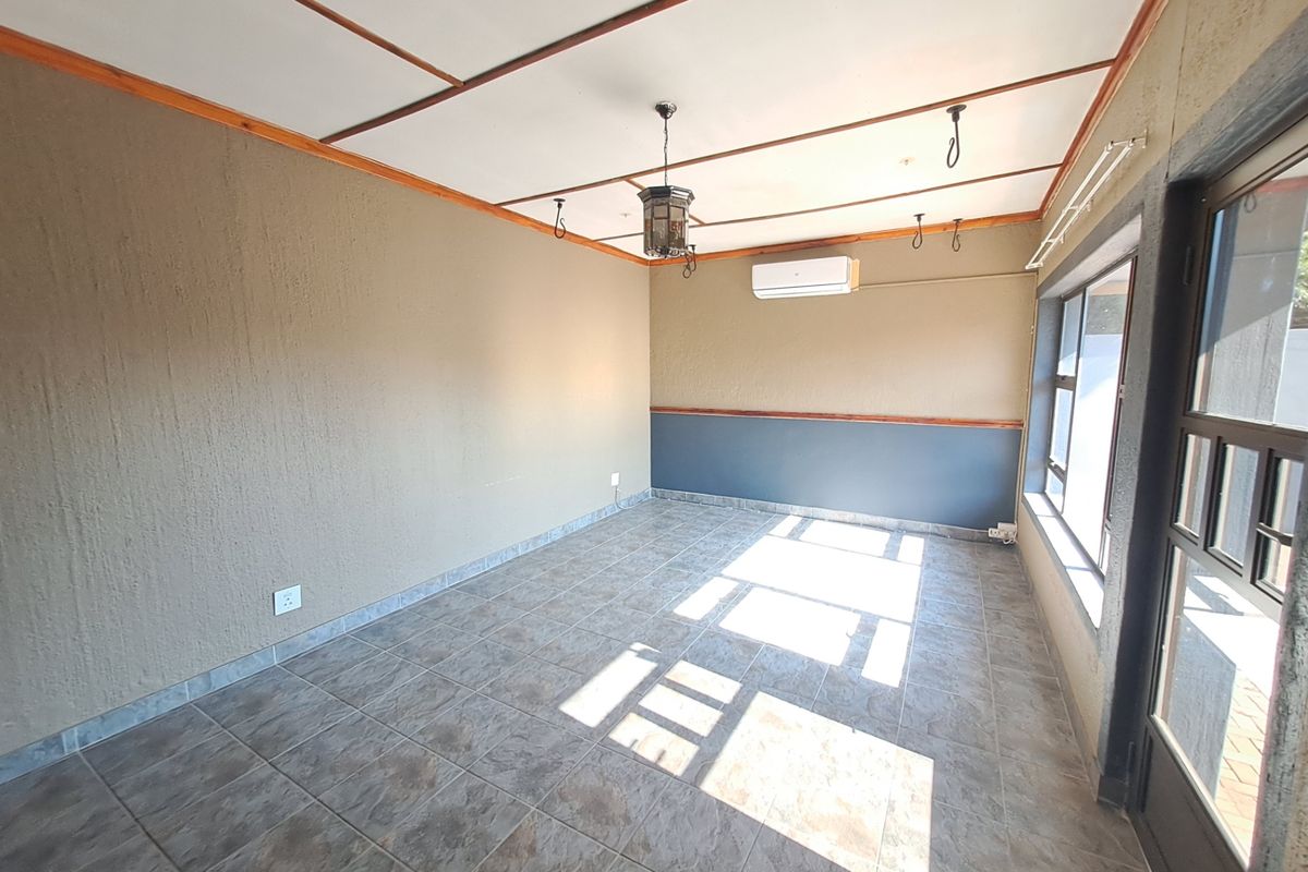 An empty living room featuring tiled flooring, a split-system air conditioner, and timber ceiling detailing, offering a clean and versatile space.