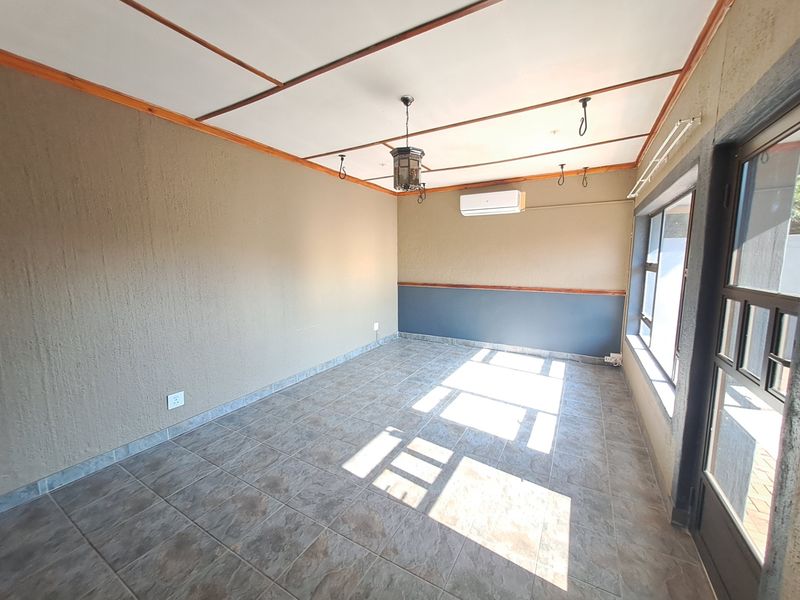 An empty living room featuring tiled flooring, a split-system air conditioner, and timber ceiling detailing, offering a clean and versatile space.