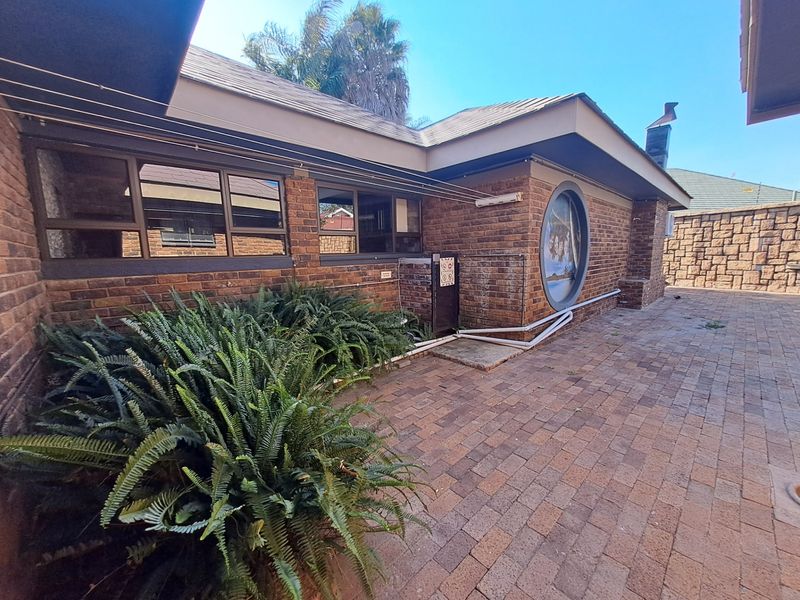 Rear exterior view of the house featuring a paved patio area, brick facade, and distinctive circular window detail.