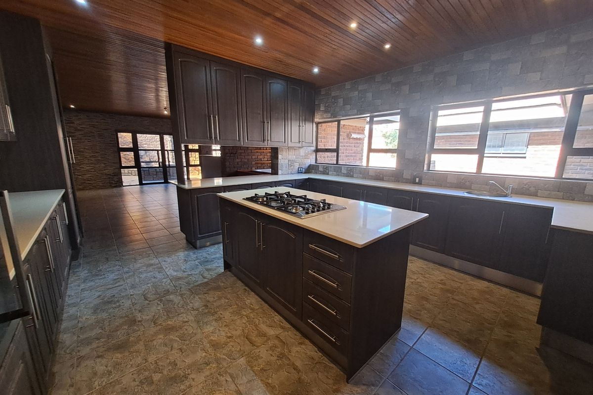 Spacious kitchen featuring a central island with gas hob, dark cabinetry, stone countertops, timber ceiling, and tiled flooring, offering a modern and functional layout.