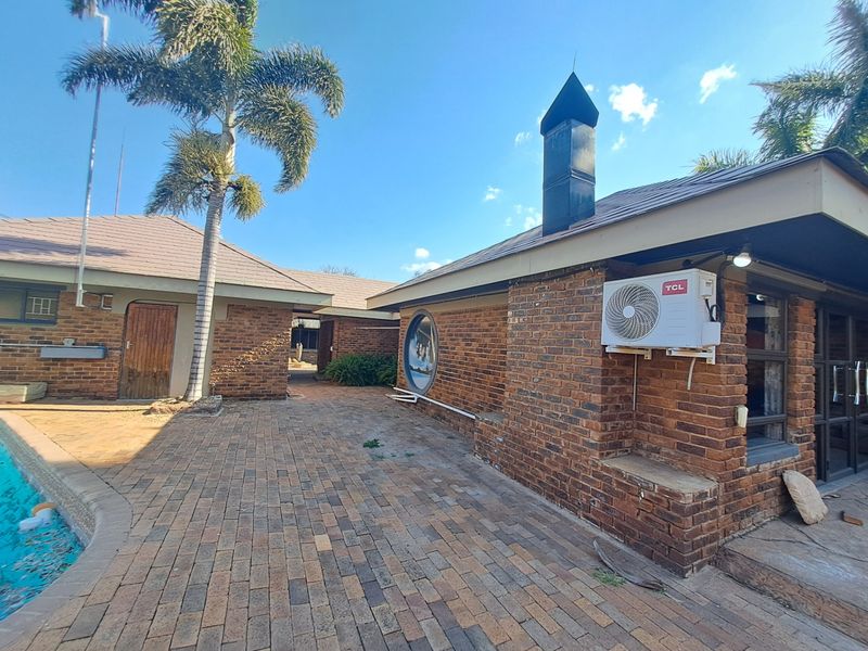 Rear exterior view featuring a brick facade, paved patio area, swimming pool, and an integrated chimney stack.
