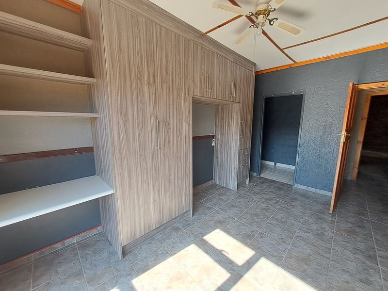 A spacious bedroom featuring extensive built-in cabinetry, tiled flooring, and a ceiling fan, offering a functional layout ready for personalization.