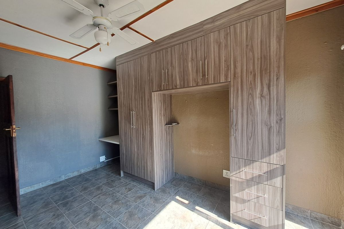 A bedroom featuring built-in wooden cupboards, a built-in desk area, a ceiling fan, and tiled flooring.