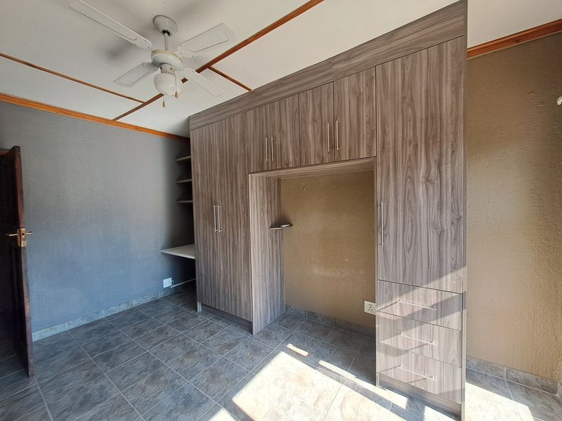 A bedroom featuring built-in wooden cupboards, a built-in desk area, a ceiling fan, and tiled flooring.