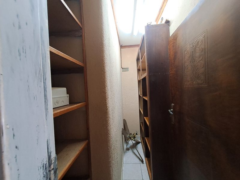 A narrow utility or storage space featuring built-in wooden shelving units and textured wall finishes, suitable for pantry or scullery use.