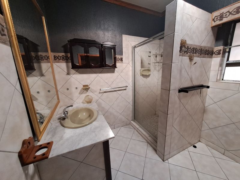 A functional bathroom featuring a shower enclosure, marble-topped vanity basin, and tiled finishes throughout.