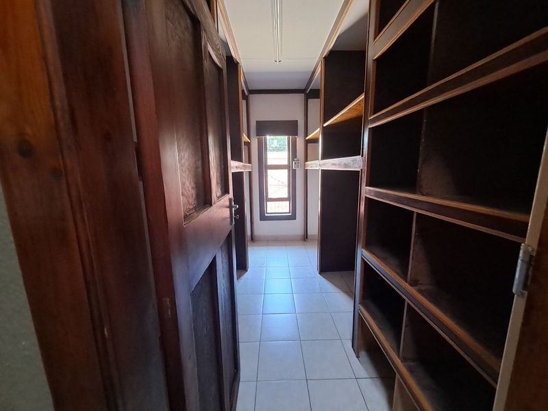 A functional walk-in storage or utility room featuring extensive built-in timber shelving and tiled flooring.