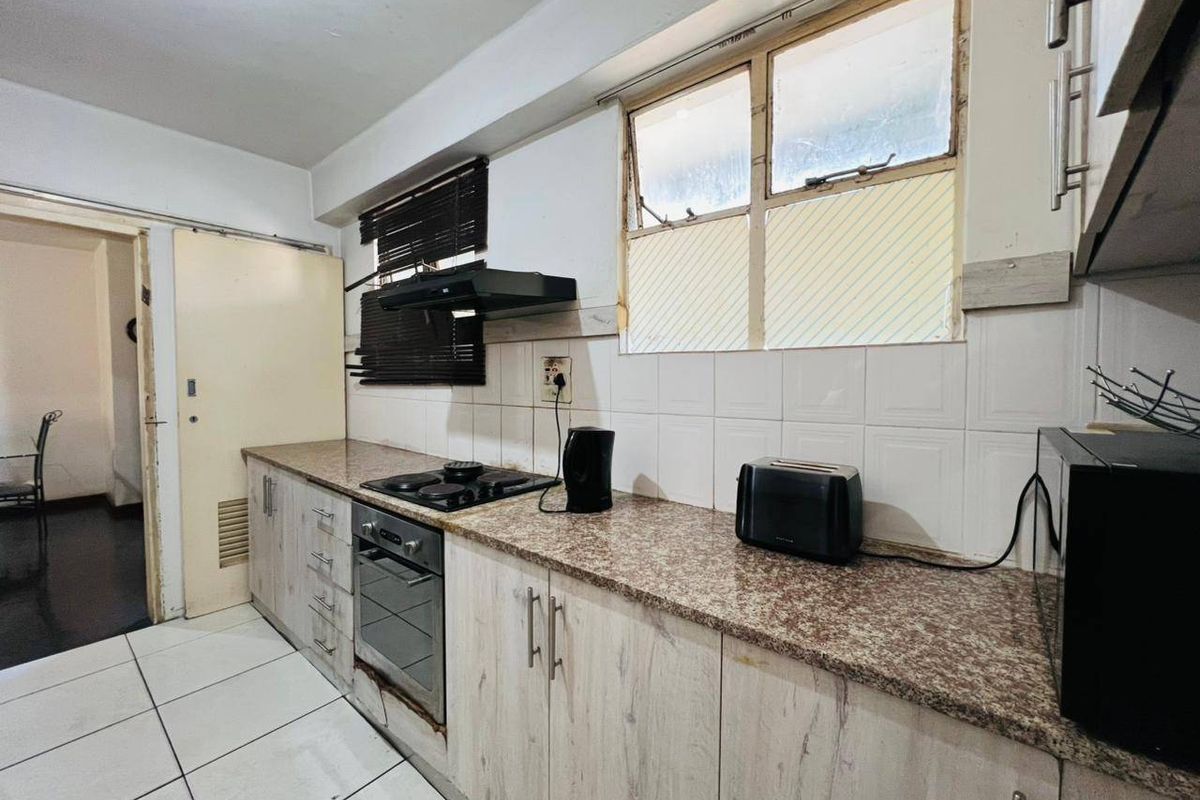 A functional kitchen featuring granite countertops, built-in cabinetry, an electric hob, and an oven, with tiled flooring and splashbacks.