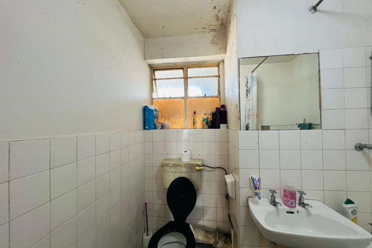 A dated bathroom featuring original ceramic tiling, a pedestal basin, and a toilet, requiring significant renovation and repair to address ceiling and wall damage.