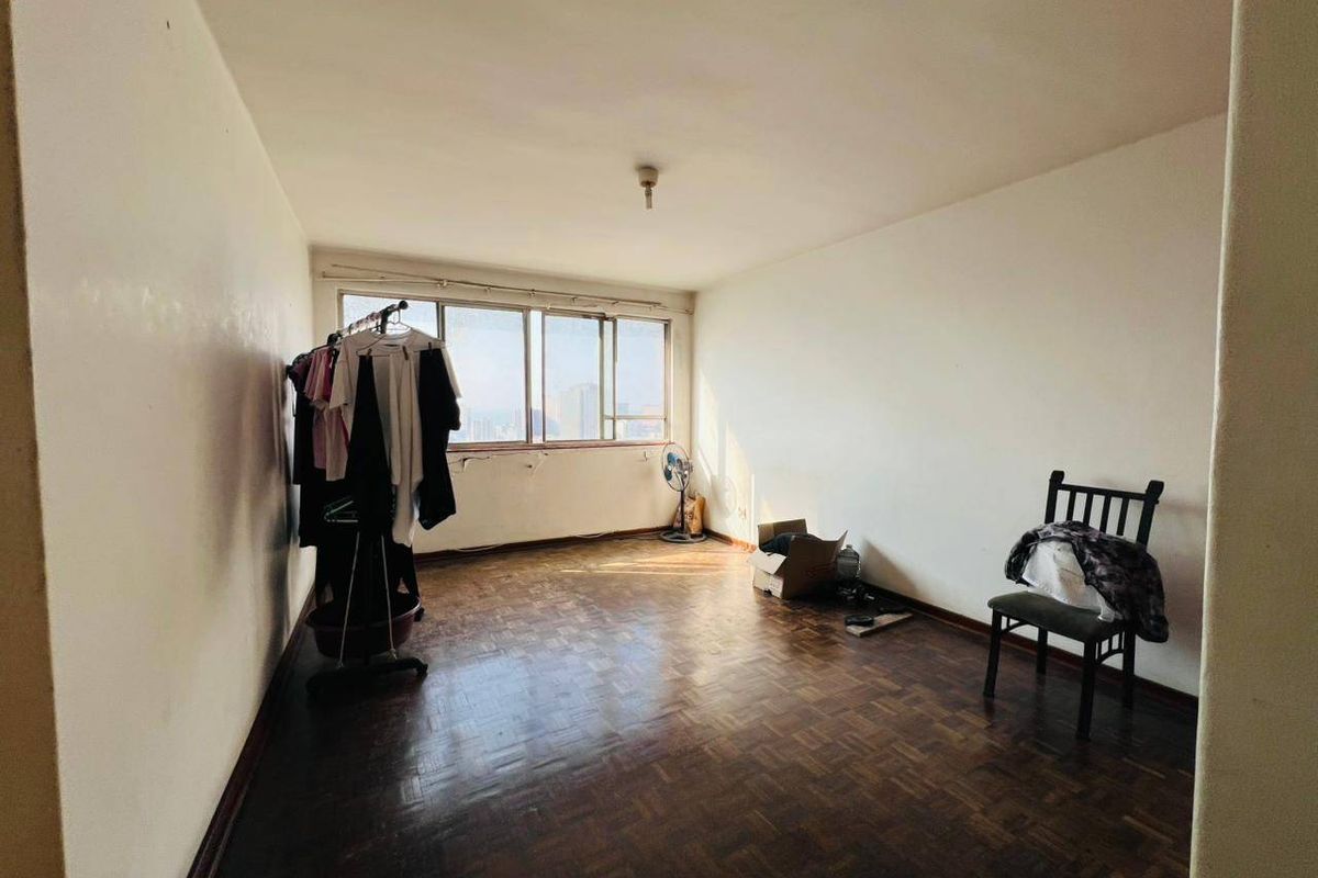 A vacant living room featuring original parquet flooring and a large window with natural light, offering a blank canvas for renovation.
