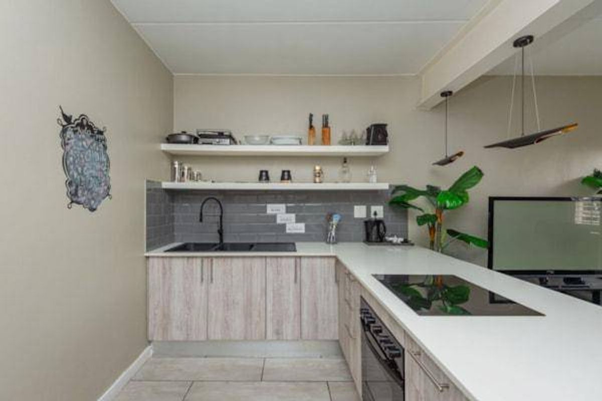 Modern kitchen featuring light wood-grain cabinetry, white countertops, subway tile backsplash, integrated hob and oven, and stylish floating shelving.
