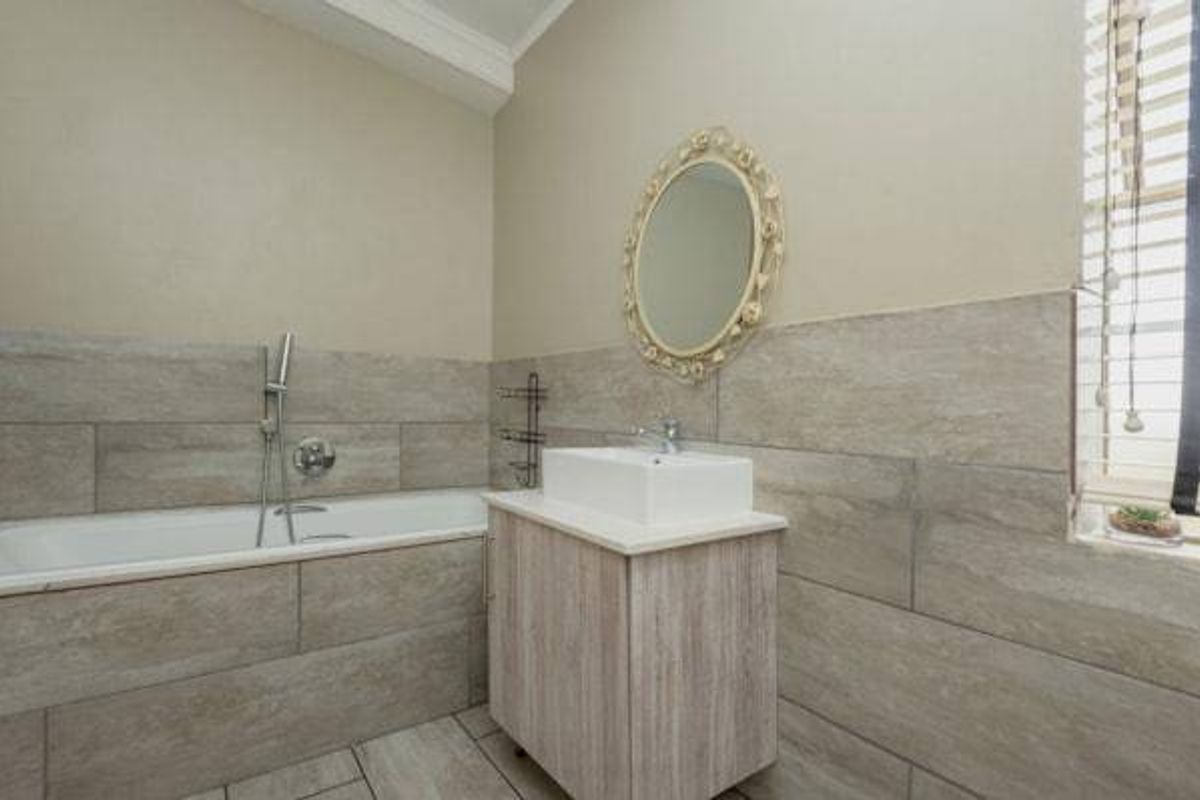 A modern bathroom featuring a built-in bathtub, a vanity cabinet with a vessel sink, and neutral-toned wall and floor tiling.