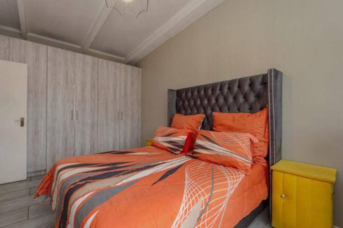A well-maintained bedroom featuring built-in cupboards, tiled flooring, and exposed ceiling beams, providing a functional and clean living space.