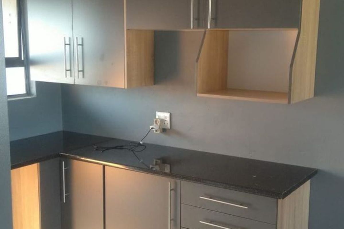 A modern, compact kitchen featuring grey and wood-tone cabinetry, dark granite countertops, and neutral tiled flooring.