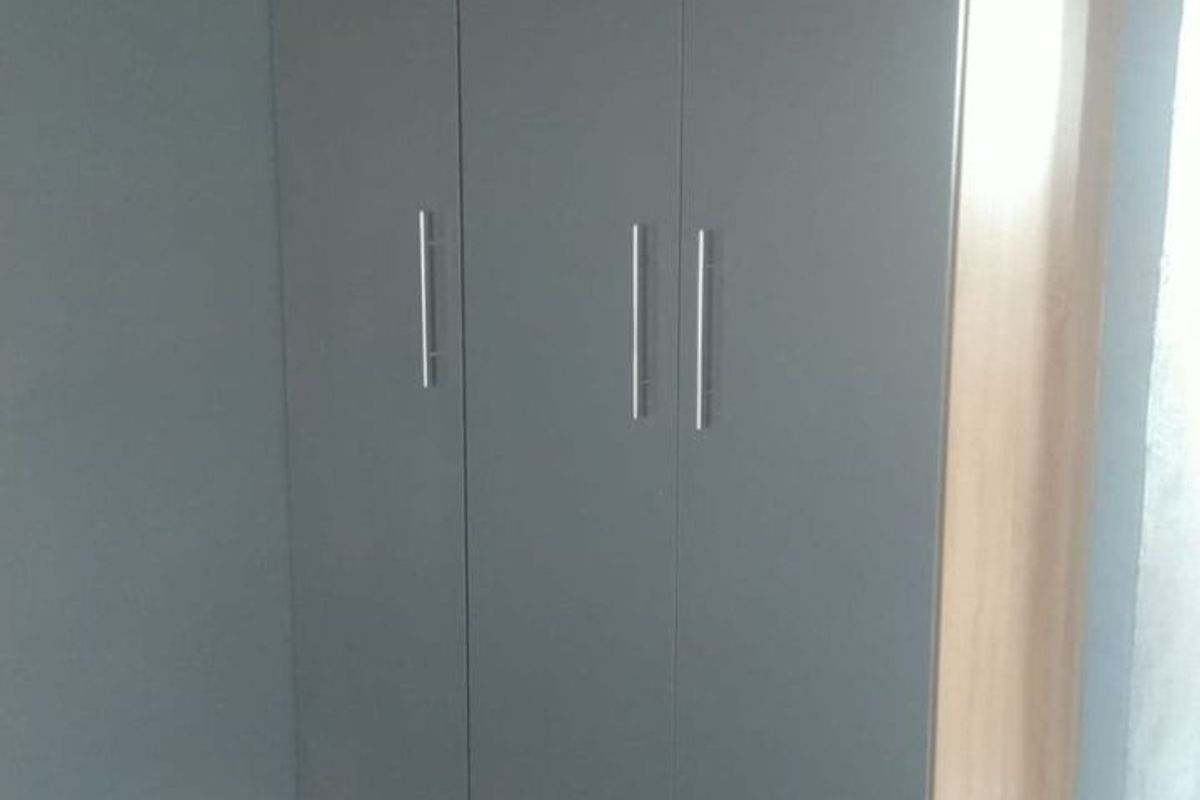 A bedroom featuring a modern, full-height built-in wardrobe with grey doors and wood-look trim.